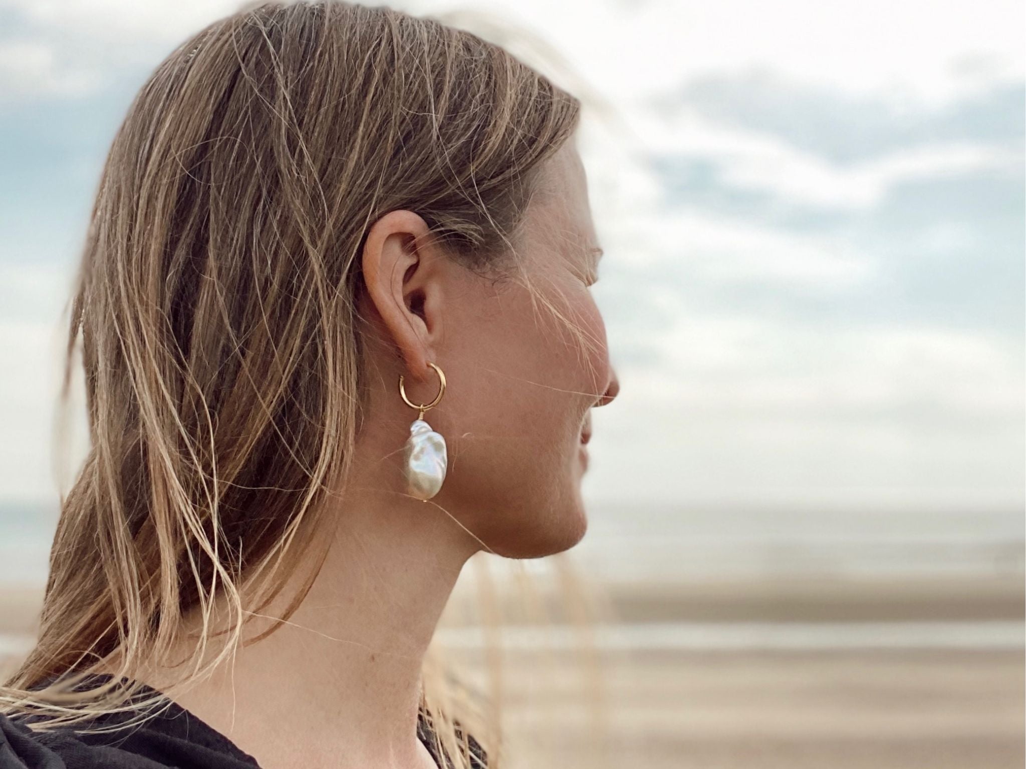 Image of the founder of RAW Copenhagen overlooking the sea at Camber Sands wearing minimalist hoop design with big freshwater baroque pearls