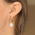 A close-up image of a woman's ear wearing a gold hoop earring with a baroque pearl attached to it.