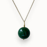 Big green round onyx pendant on a gold chain, photographed on an off white background