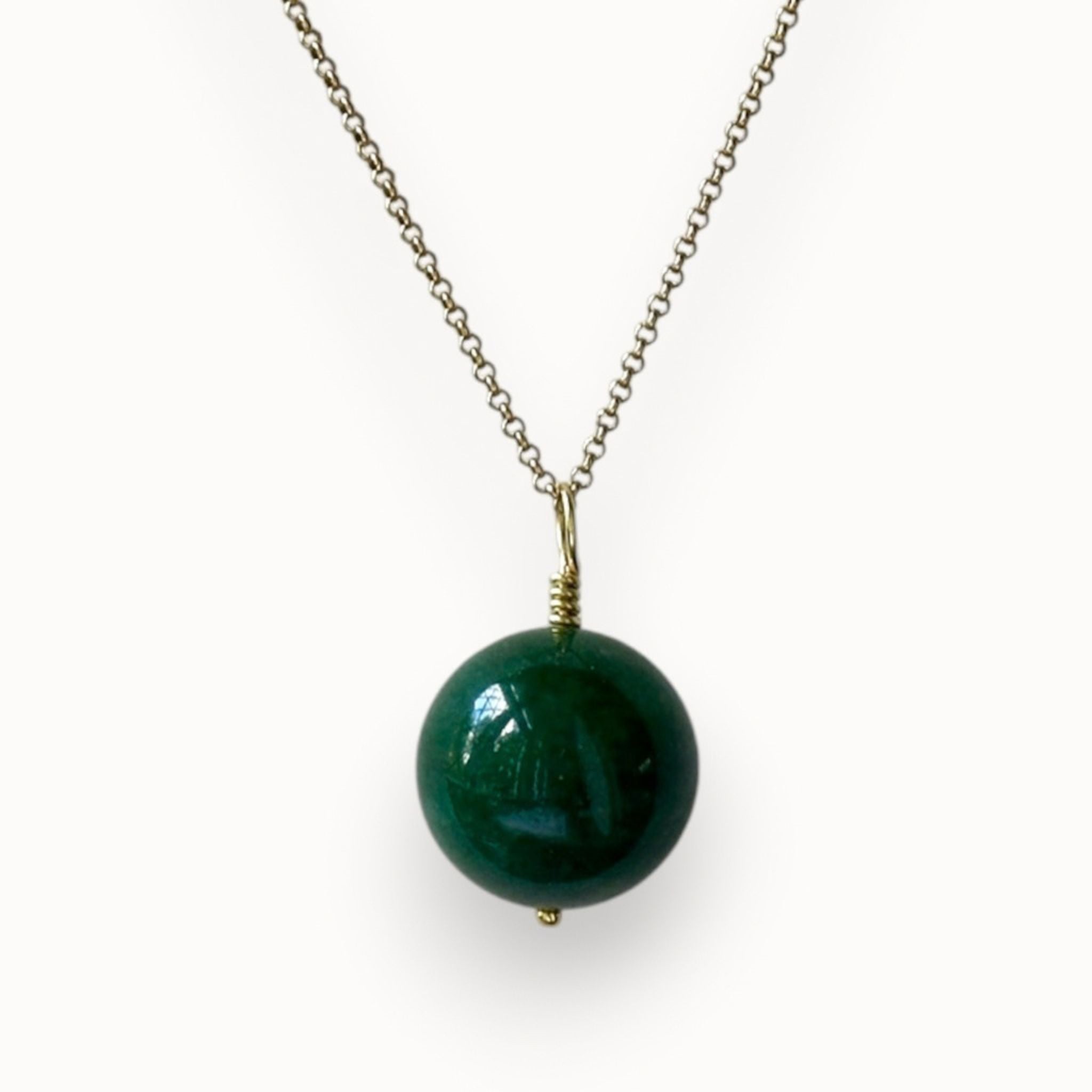 Big green round onyx pendant on a gold chain, photographed on an off white background