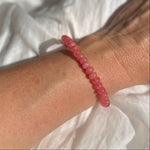 Close-up of a wrist wearing a pink beaded bracelet against a white fabric background