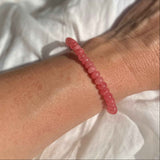 Close-up of a wrist wearing a pink beaded bracelet against a white fabric background