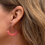 Close-up of an ear wearing a pink jade beaded hoop earring with blonde hair.