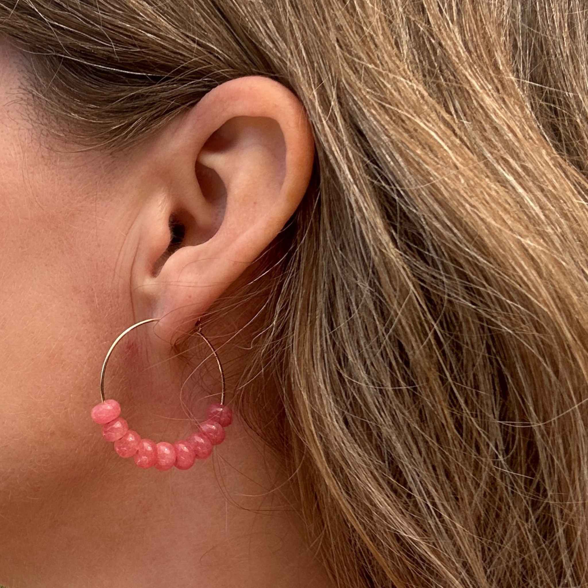 Close-up of an ear wearing a pink jade beaded hoop earring with blonde hair.