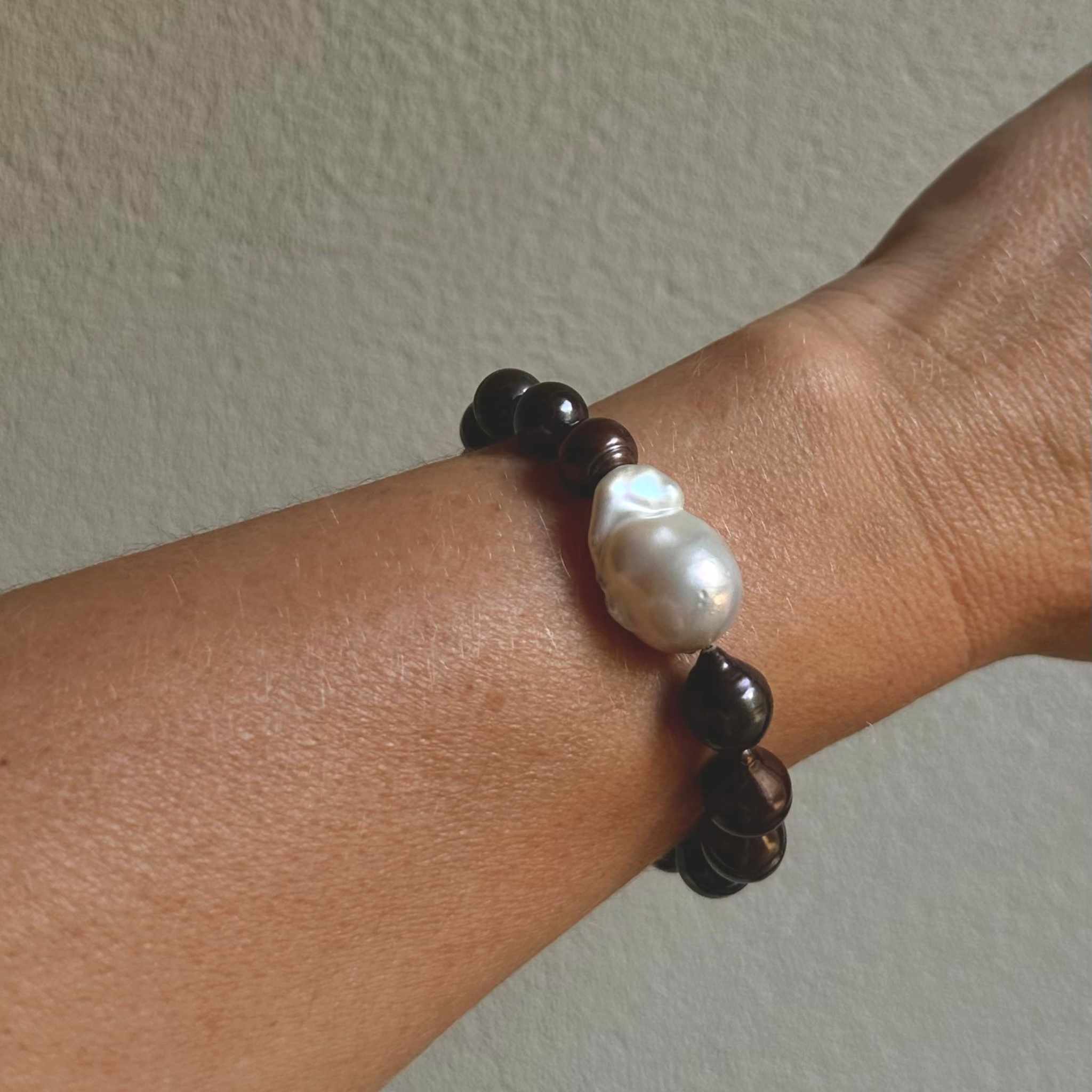 Bracelet with brown pearls  and a focal white baroque earl on a wrist against a plain background