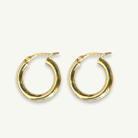 Chunky gold hoops from RAW Copenhagen resting on a linen coloured background
