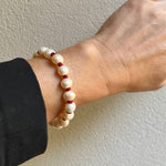 A beaded stretch bracelet with cream-colored round beads and small red spacer beads, shown worn on a person's wrist with a black sleeve visible.