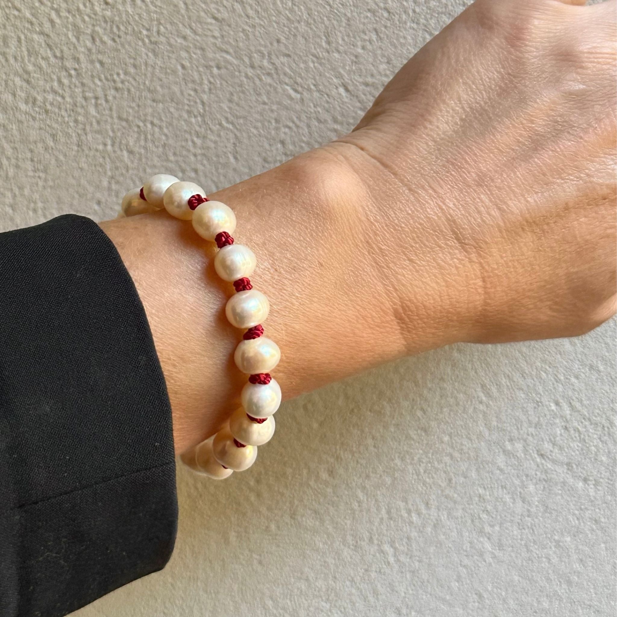 A beaded stretch bracelet with cream-colored round beads and small red spacer beads, shown worn on a person's wrist with a black sleeve visible.