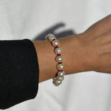 A close-up of a person's wrist wearing a beaded bracelet made of white pearl-like beads separated by small red spacer beads, with a black sleeve visible at the edge.