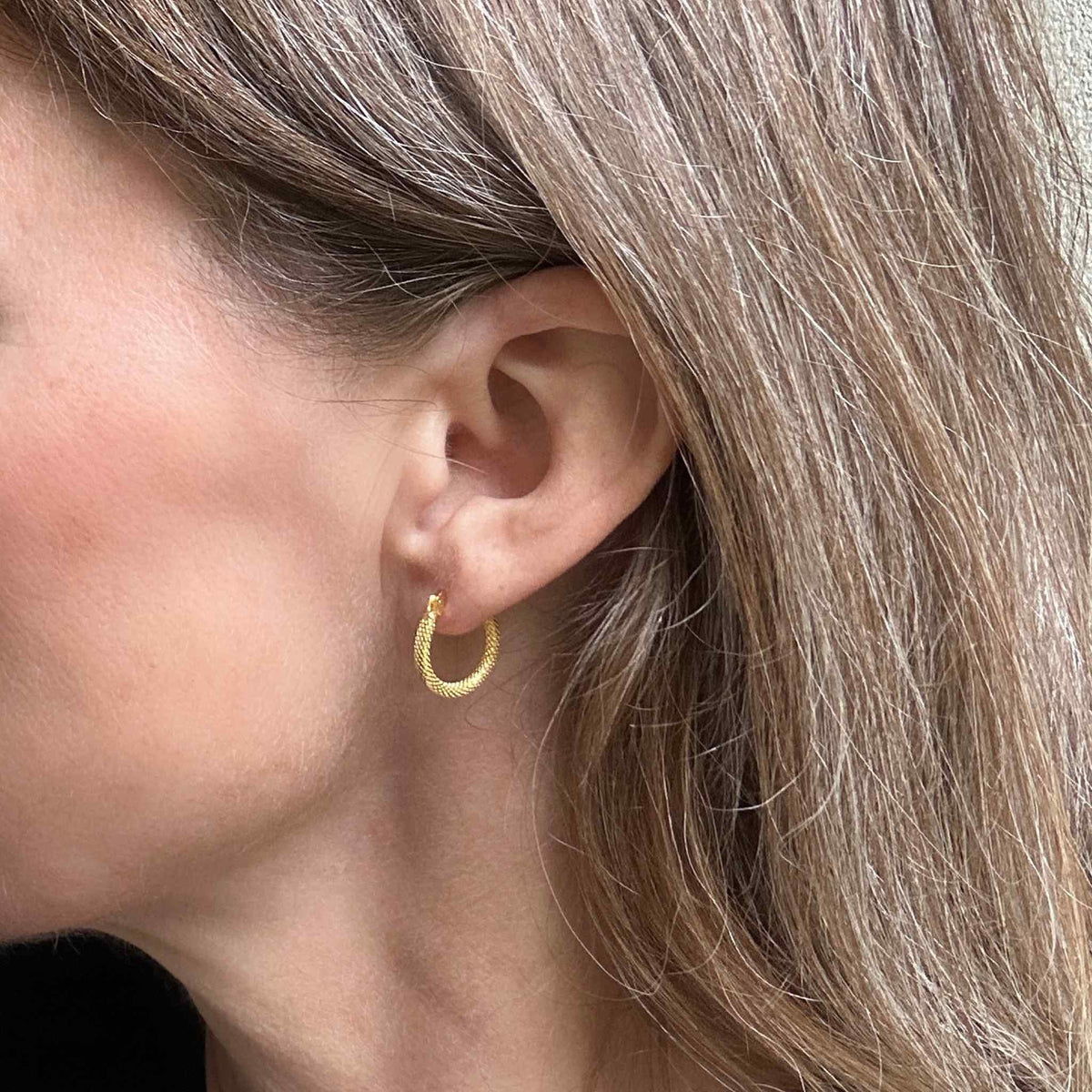 delicate small gold hoops modelled for size against dark blond long hair