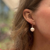 Close-up of an ear wearing a pearl earring with a blurred natural background
