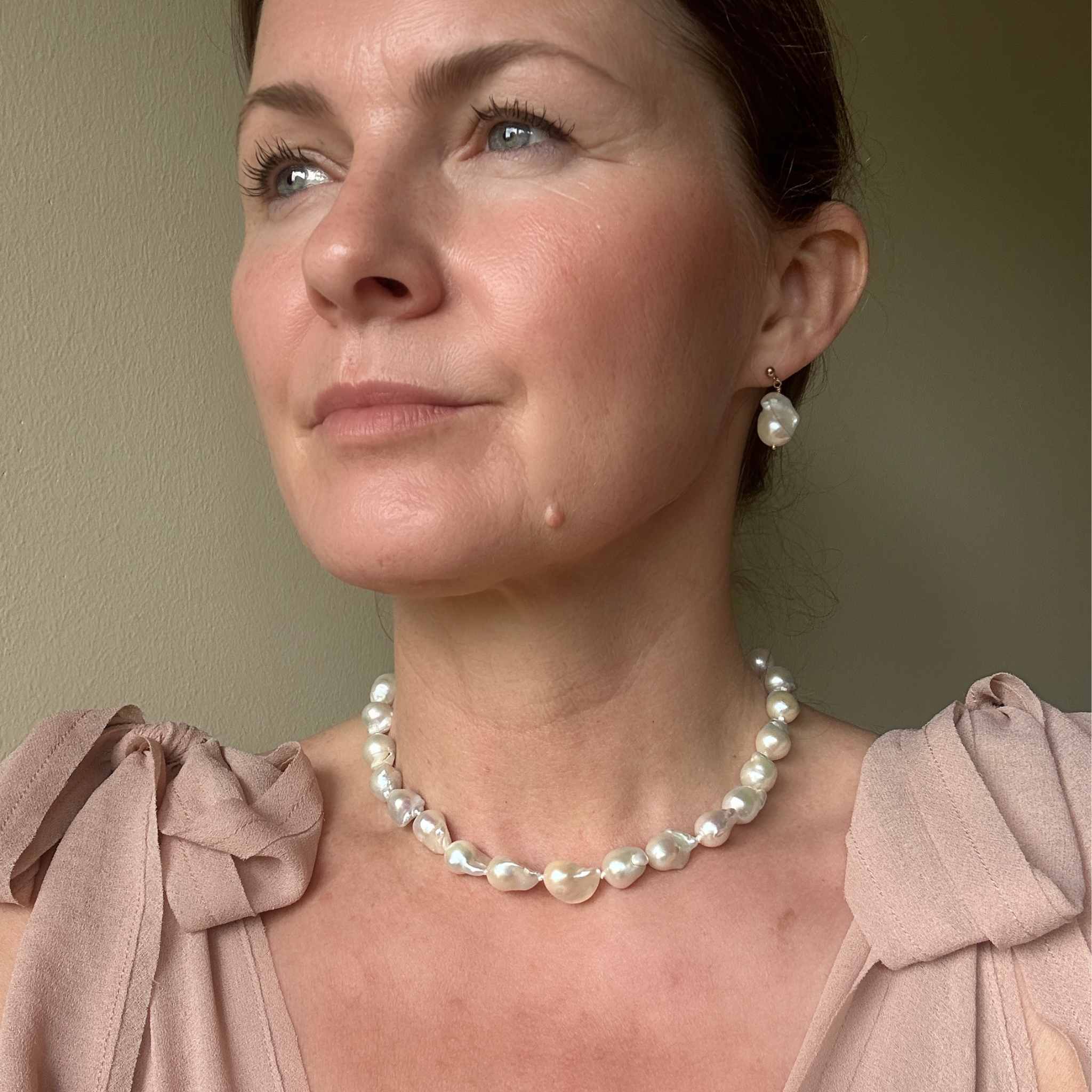 Baroque pearl necklace and earrings modelled against a dusty pink wedding guest dress