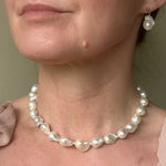 Medium sized baroque pearl necklace and earrings on a person against a neutral background