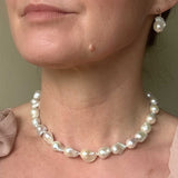 Medium sized baroque pearl necklace and earrings on a person against a neutral background