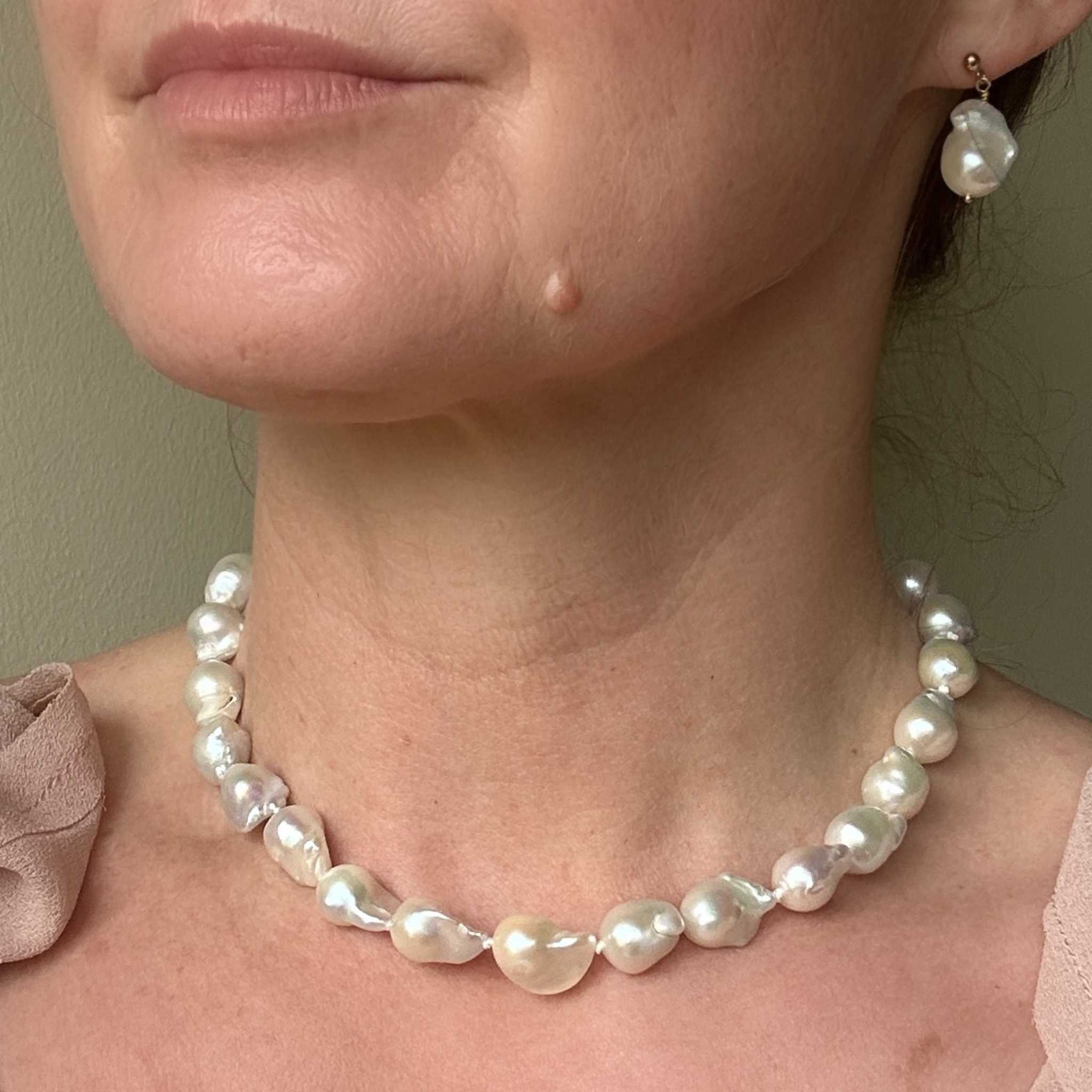 Medium sized baroque pearl necklace and earrings on a person against a neutral background