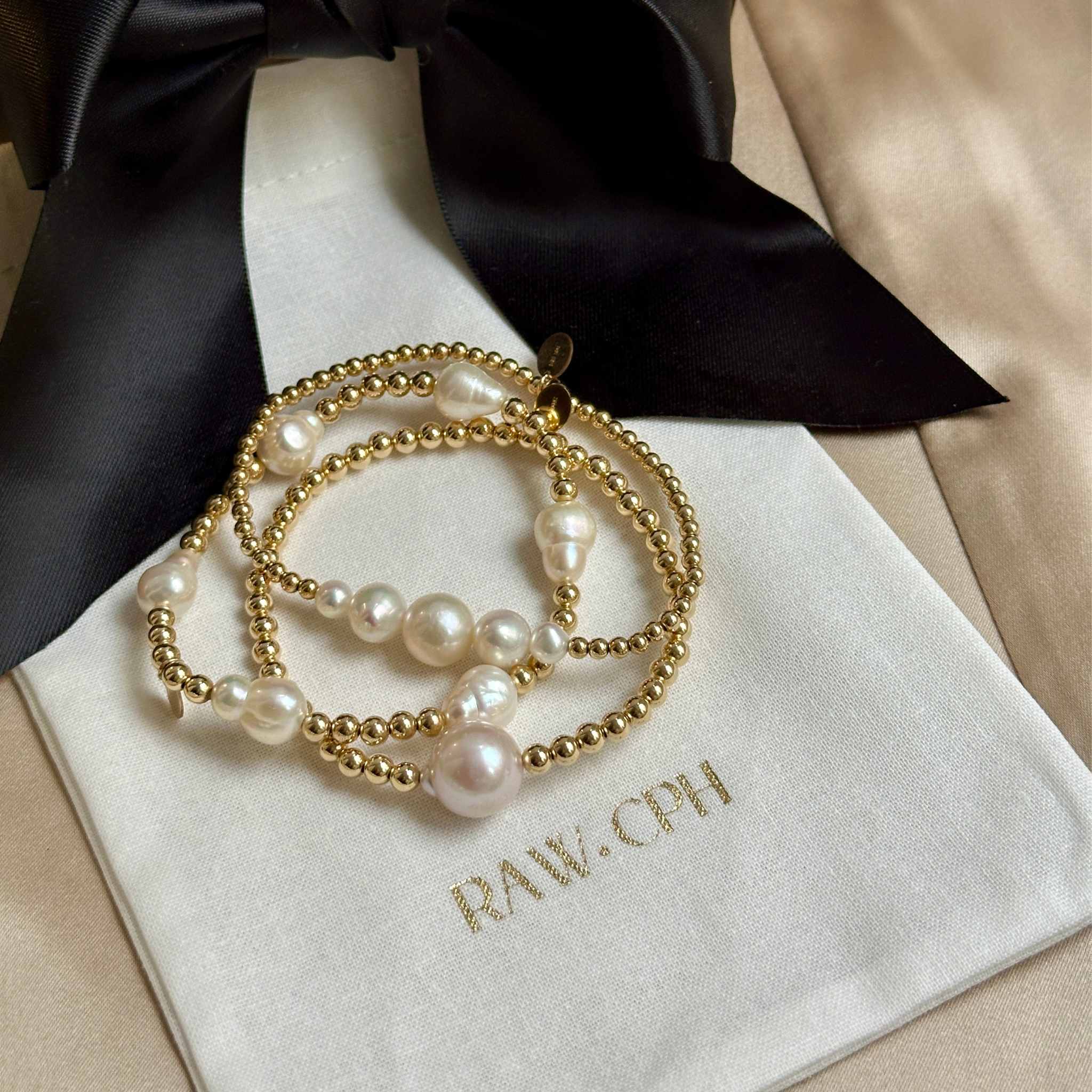 Pearl and gold bracelet on a cream jewellery pouch with 'RAW.CPH' branding