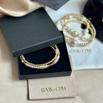 Pearl and gold bracelet in a black box with 'RAW.CPH' branding on a beige fabric background.