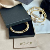 Pearl and gold bracelet in a black box with 'RAW.CPH' branding on a beige fabric background.