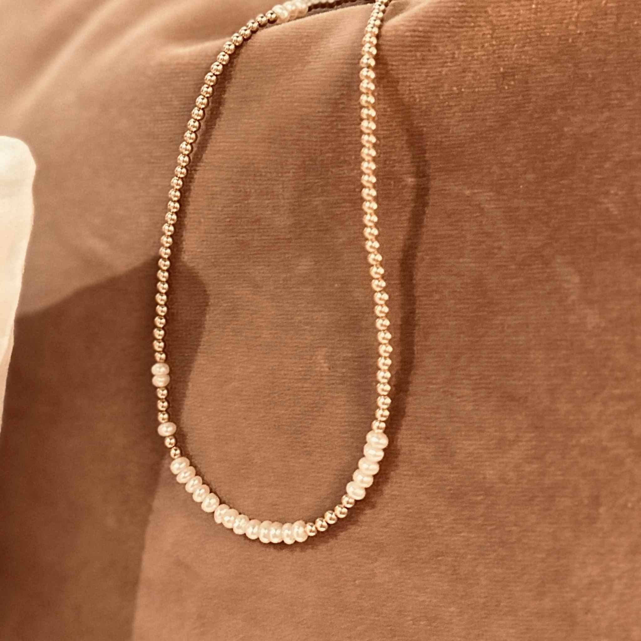 Gold wrap bracelet with pearls that doubles as a necklace on a rust velvet background 