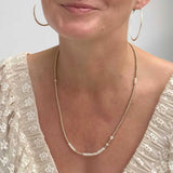 Woman wearing a gold-filled and pearl necklace with a plain background