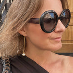 Woman wearing RAW Copenhagen long pearl gold earrings and large sunglasses with a blurred background