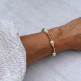 Gold filled beaded bracelet with double freshwater pearls modelled on sun-kissed skin with a ballon  sleeved dress, arm resting 