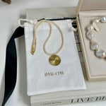 Pearl necklace with gold pendant on a branded pouch, with a jewelry box in the background.