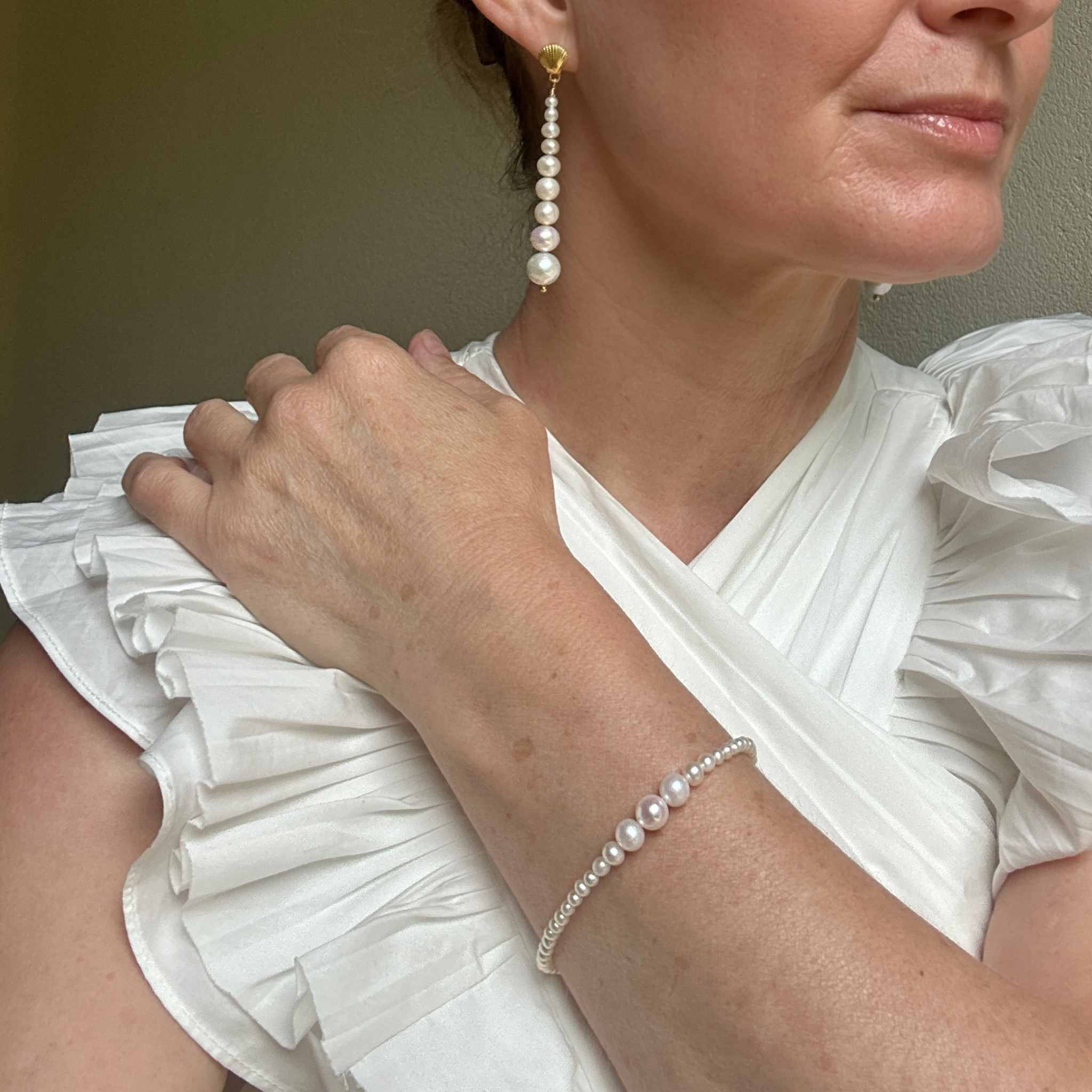 Woman wearing pearl earrings and bracelet against a neutral background