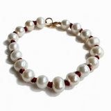 A strand of irregular white freshwater pearls threaded with dark red cord and accented with small gold beads, finished with a gold lobster clasp, shown on a white background.