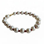 A beaded bracelet featuring large, lustrous white freshwater pearls separated by small dark red cord accents and finished with a gold clasp, shown on a plain white background.