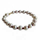A beaded bracelet featuring large, lustrous white freshwater pearls separated by small dark red cord accents and finished with a gold clasp, shown on a plain white background.
