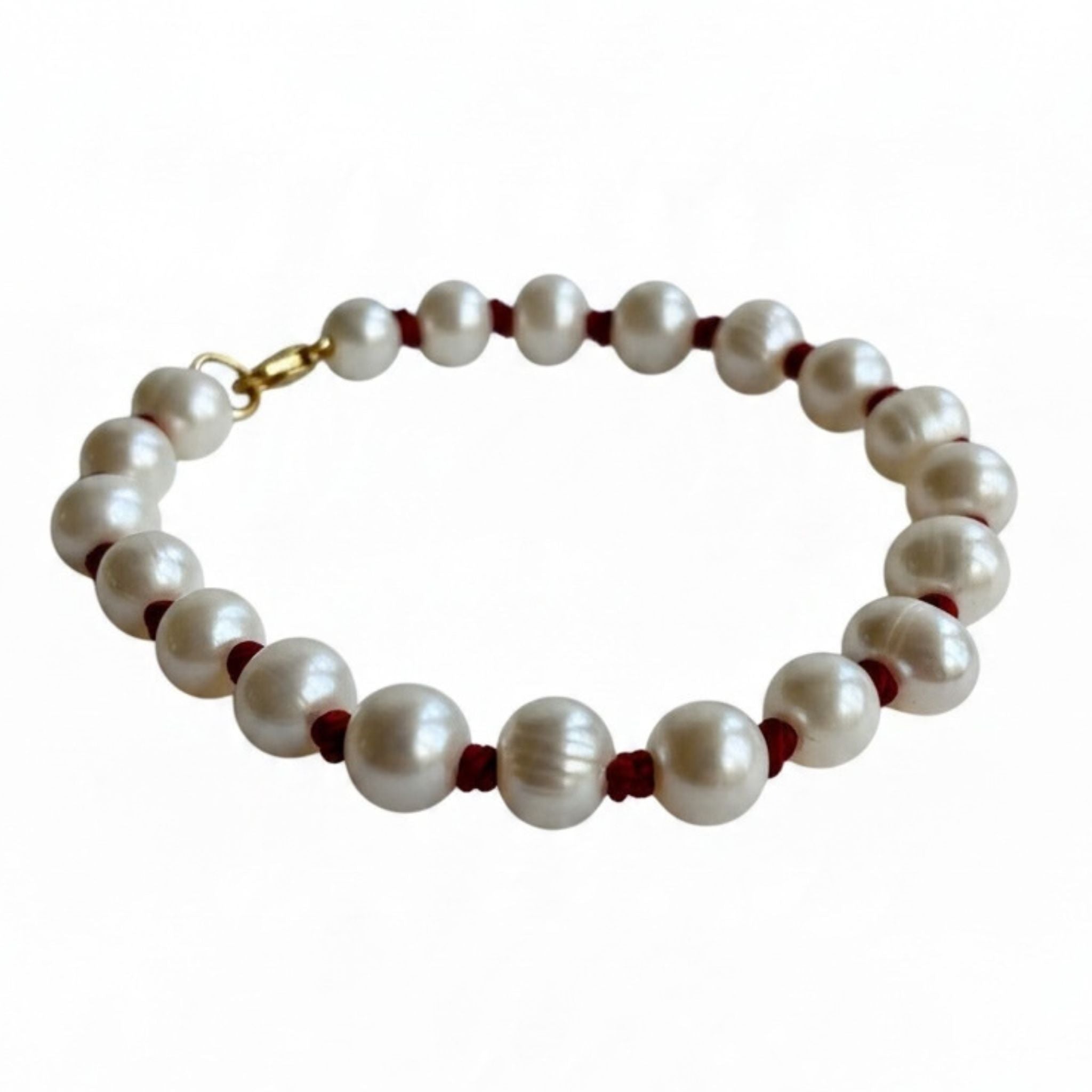 A beaded bracelet featuring large, lustrous white freshwater pearls separated by small dark red cord accents and finished with a gold clasp, shown on a plain white background.
