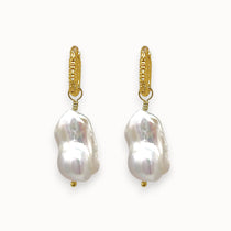 Pair of big white baroque pearl earrings with gold textured huggies
 on a white background