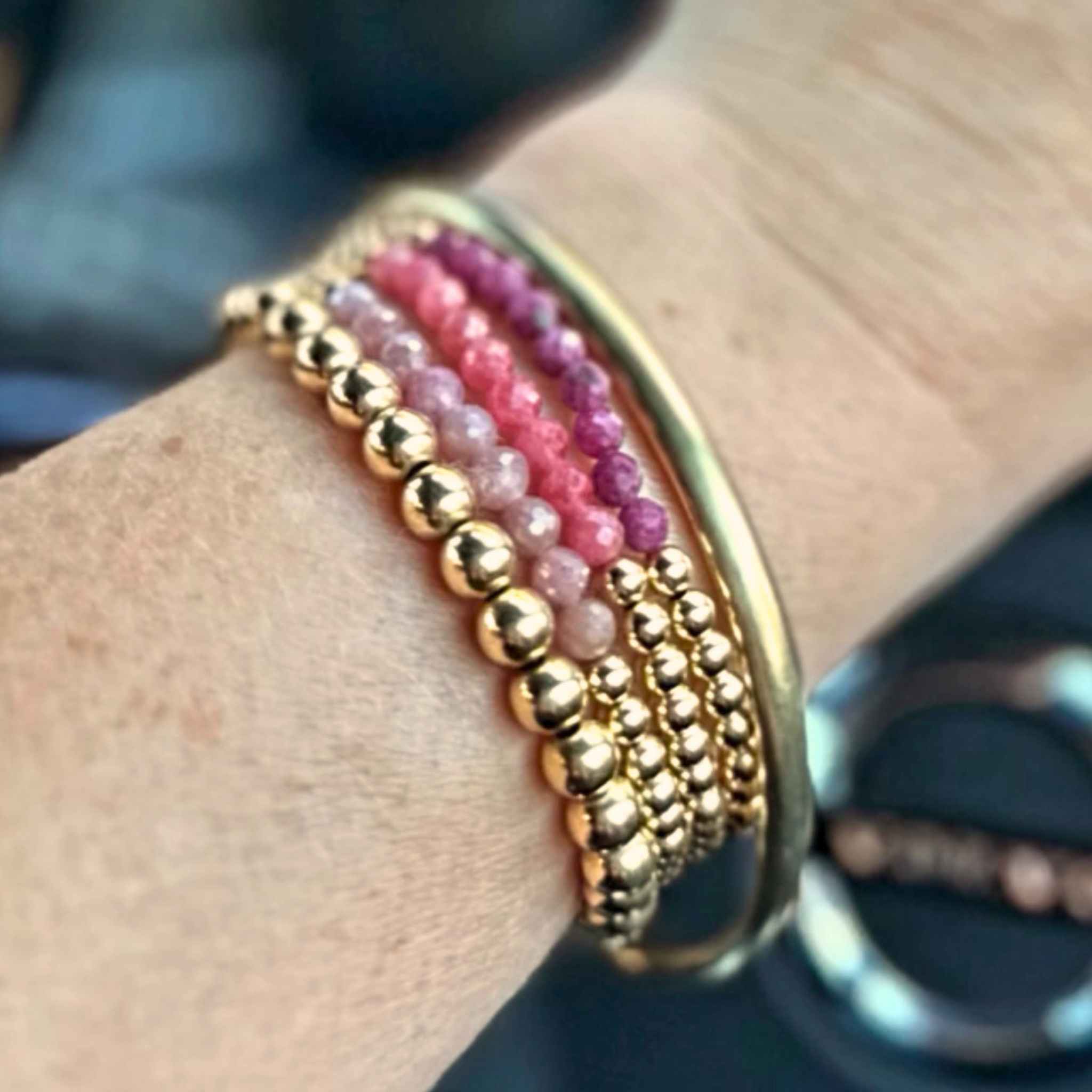 Gold and pink beaded bracelet on a wrist with a blurred background