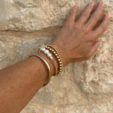 Hand wearing gold and pearl bracelets against a stone wall background