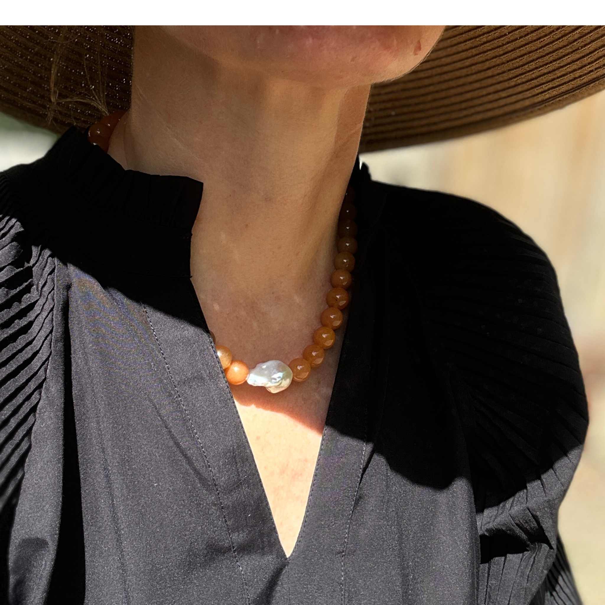 Red aventurine and baroque pearl statement necklace modelled against black v-neck cotton dress