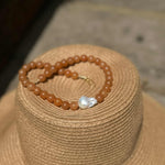 Red aventurine and baroque pearl statement necklace resting on big summer straw har