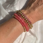 Close-up of a wrist wearing pink beaded bracelets with gold accents on a white background