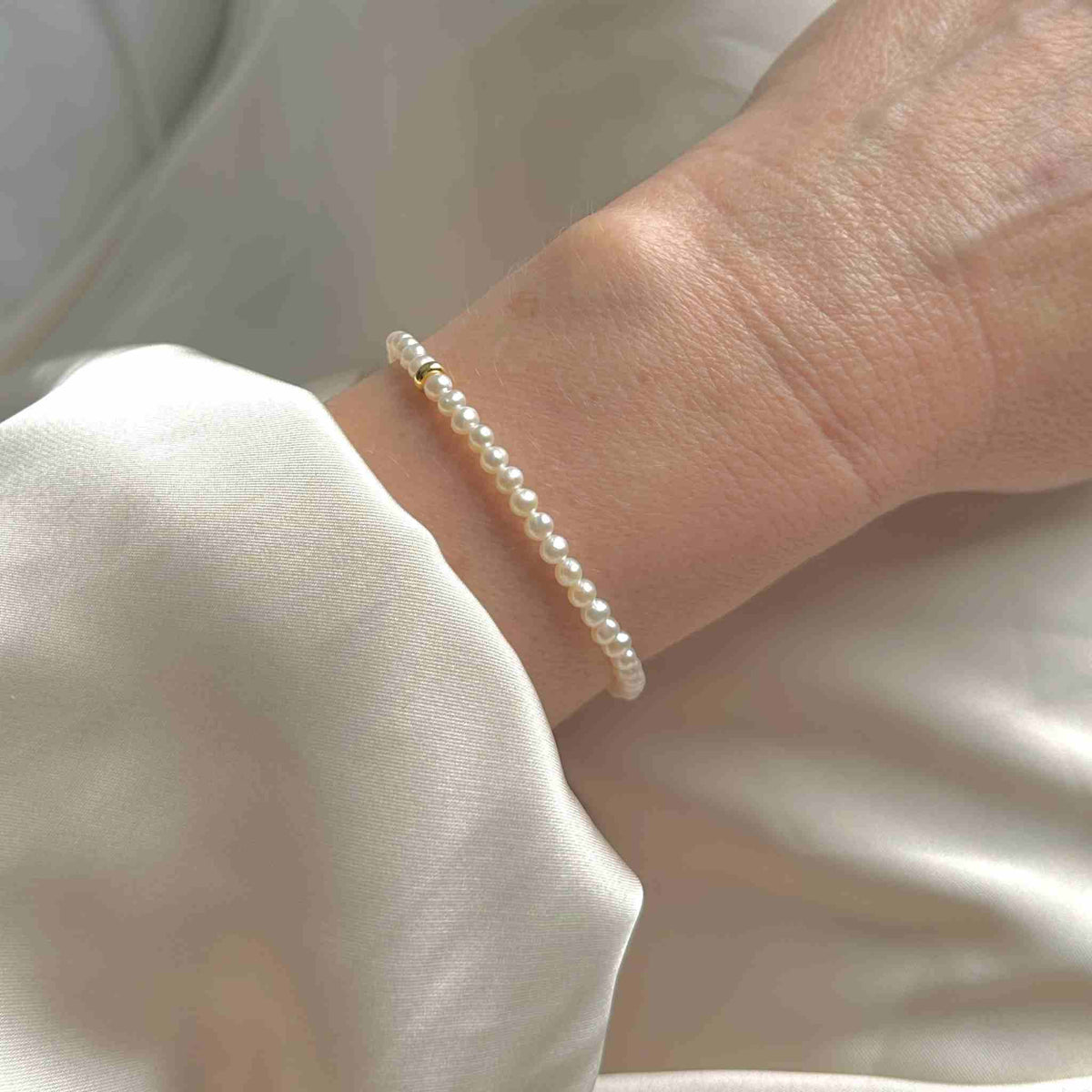 Small round pearl bracelet gold accent modelled on wrist with cream silk wedding dress