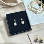 Pearl earrings on a black jewelry box with a pearl necklace in the background.