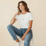 Woman wearing a white t-shirt and blue jeans sitting on a white stool against a beige background