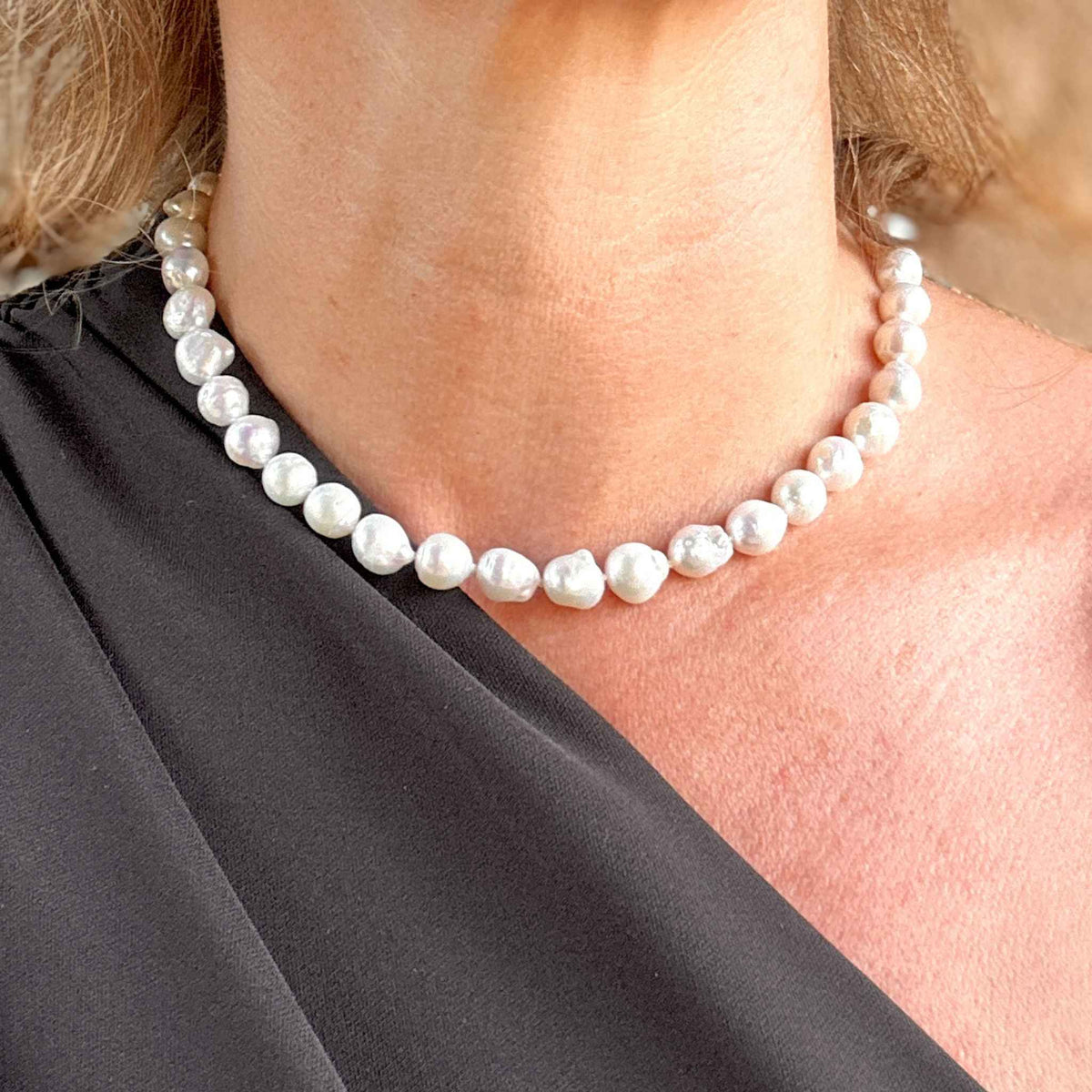 Stunning baroque pearl necklace with round gold clasp modelled against a one sleeved black dress