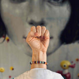 The RAW Charity Bracelet in Support of Amnesty International  with multicoloured gemstones modelled against a painting with knotted fist