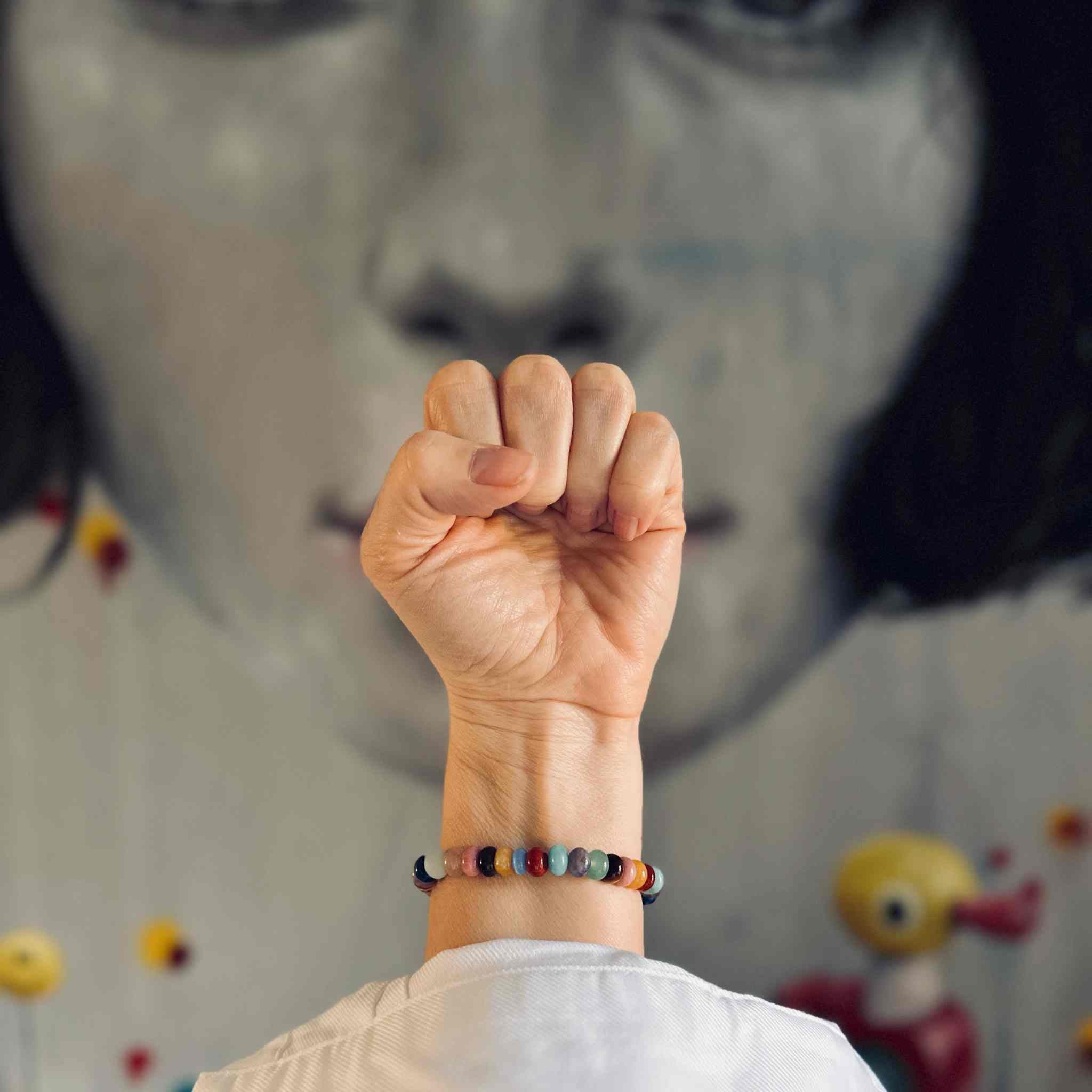 The RAW Charity Bracelet in Support of Amnesty International  with multicoloured gemstones modelled against a painting with knotted fist