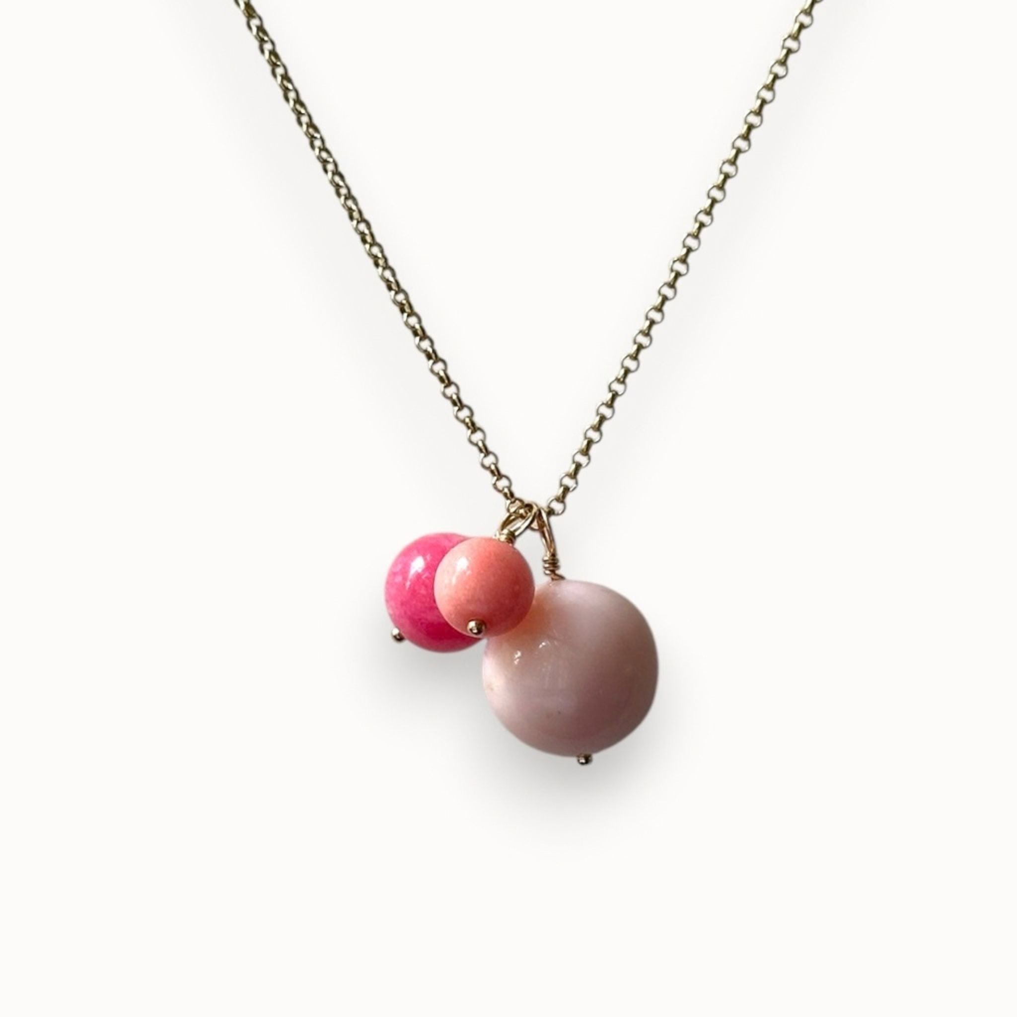 A delicate necklace featuring a gold-toned chain with a pendant consisting of two small pink beads and one larger, smooth matte pink stone bead, shown against a plain white background.