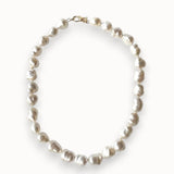 A strand of irregular white baroque pearls arranged in an oval shape, secured with a small gold clasp, shown on a clean white background.