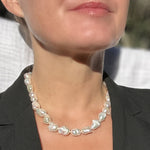 A close-up of a woman wearing a baroque pearl necklace with irregular, glossy white pearls, styled with a black blazer.