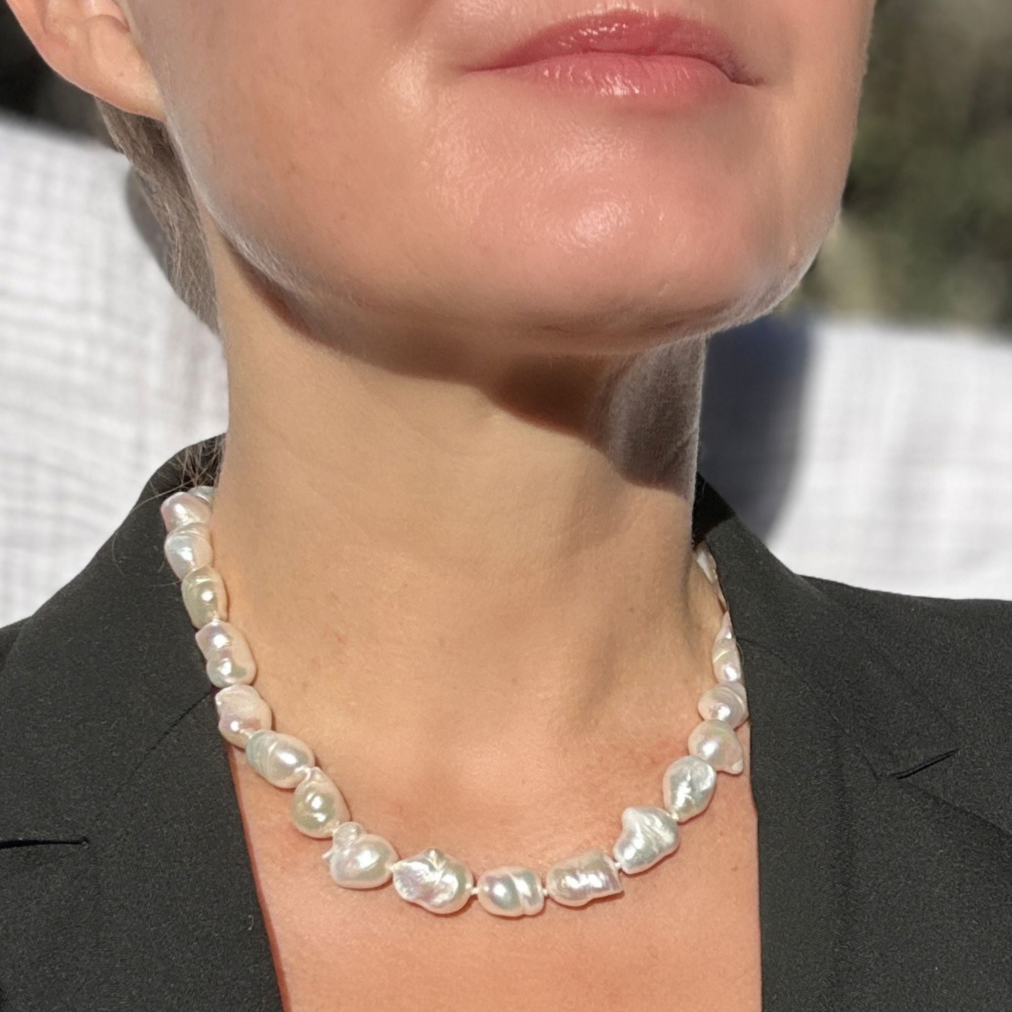 A close-up of a woman wearing a baroque pearl necklace with irregular, glossy white pearls, styled with a black blazer.