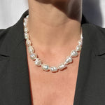 A close-up of a person wearing a baroque pearl necklace with irregular, glossy white pearls, styled with a black blazer.