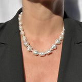 A close-up of a person wearing a baroque pearl necklace with irregular, glossy white pearls, styled with a black blazer.